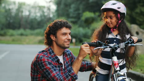 Closeup.-Portrait-of-a-little-girl-and-her-dad-next-to-the-bike.-Looking-into-the-camera.-Smiling.-Blurred-background